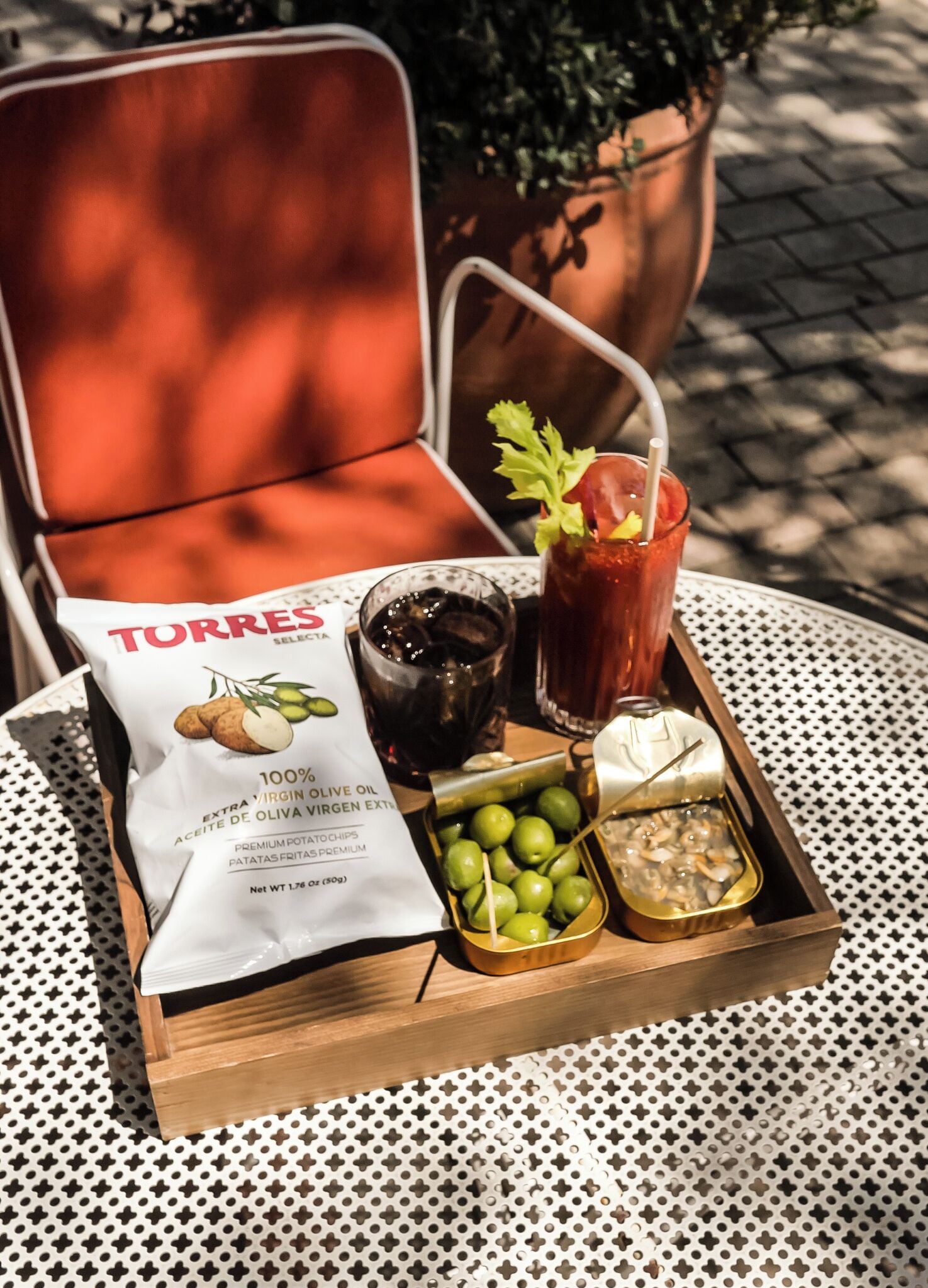 A tray with a bag of extra virgin olive oil, a glass of iced drink with a straw, a small container of olives, and a small dish of what appears to be a dip or spread.
