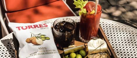 A tray with a bag of extra virgin olive oil, a glass of iced drink with a straw, a small container of olives, and a small dish of what appears to be a dip or spread.