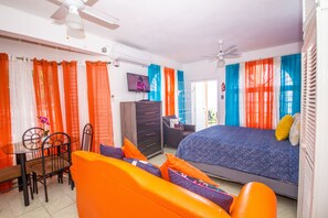 A room with a bed, a desk with a chair, a TV, and a ceiling fan. - Ocho Rios Studio Ocean View (Ocho Rios)
