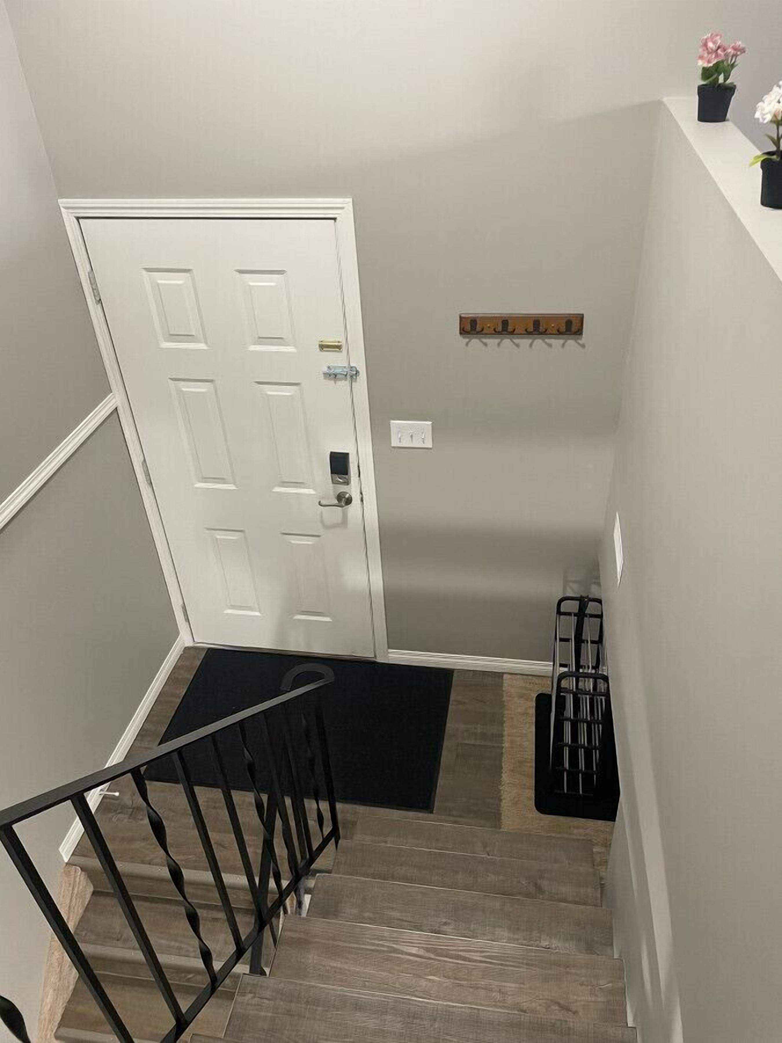 A staircase with a black railing, a white door, and a small shelf with flowers.