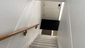 A carpeted staircase with a wooden handrail leading to a white door.