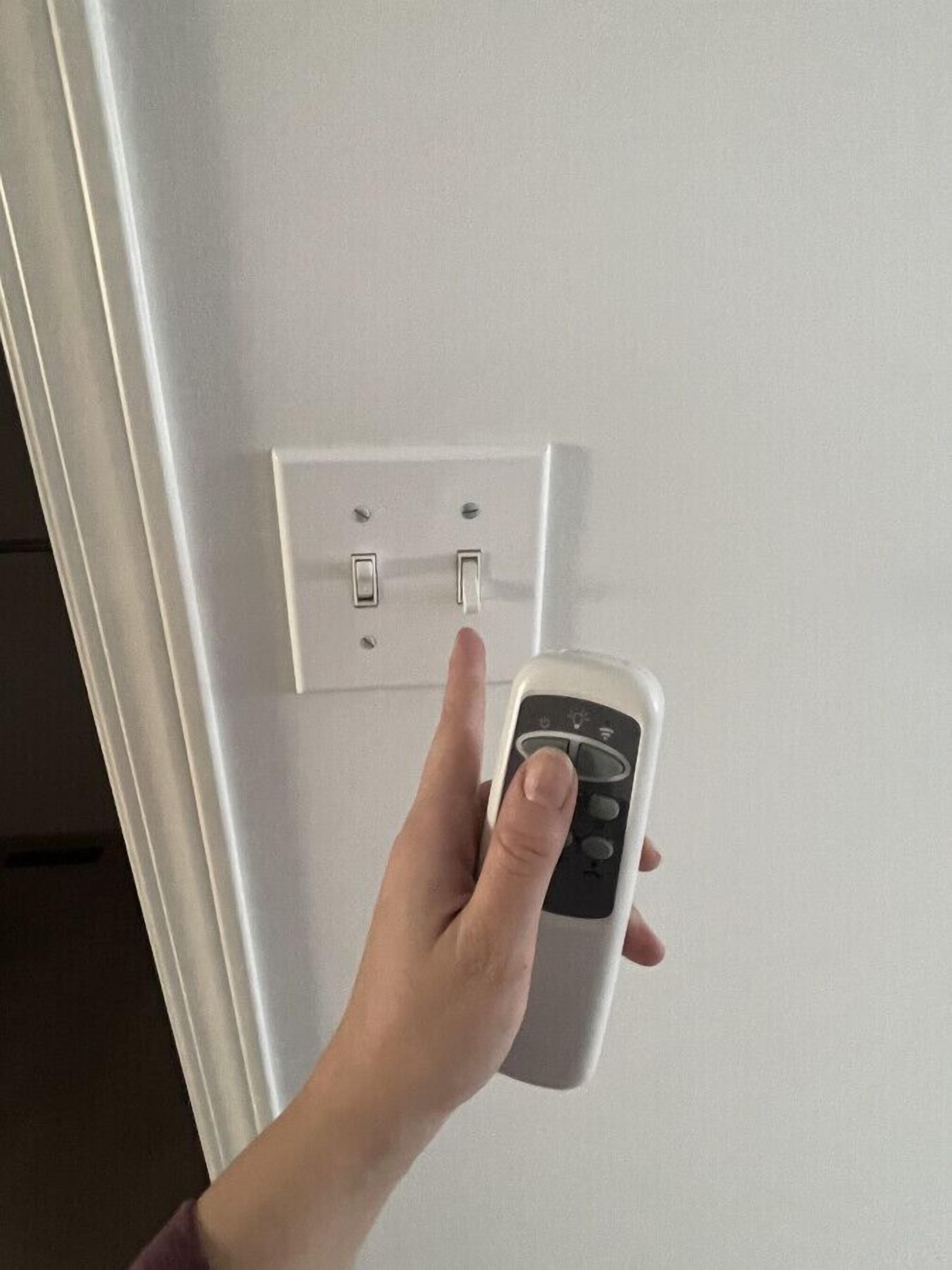 A hand using a remote control to operate a wall-mounted switch.
