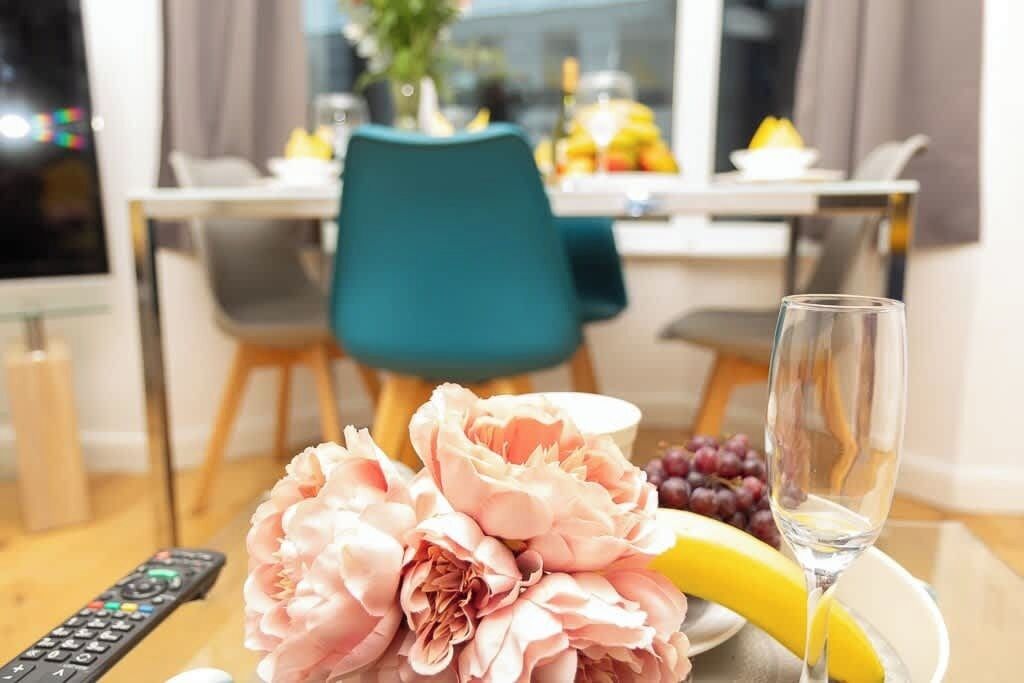 Un coin repas avec une table dressée pour deux personnes, une télécommande, un verre de vin, une banane et un bouquet de fleurs.