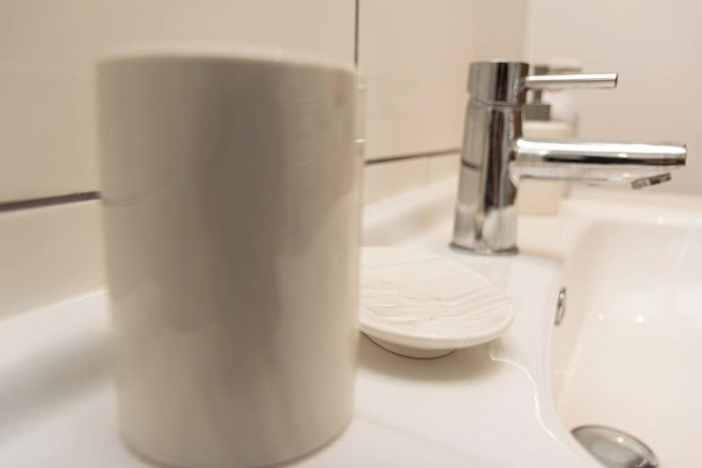 Een badkamer met een witte wastafel, een chromen kraan en een witte keramische mok.