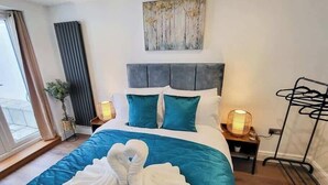 Un dormitorio moderno con una cama grande, ropa de cama color verde azulado y dos toallas blancas dispuestas en forma de cisne.