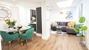 Una sala de estar moderna con un sofá gris, sillas verdes y una mesa de comedor preparada para cuatro.