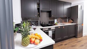 Una cocina moderna con armarios oscuros, un refrigerador de acero inoxidable y una encimera blanca con frutas y una copa de vino.