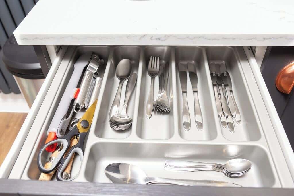 A drawer with neatly organized kitchen utensils including spoons, forks, knives, and scissors.