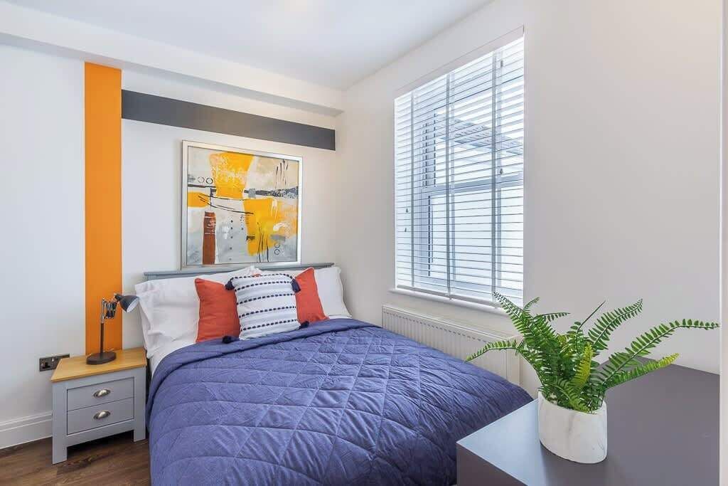 Une chambre à coucher moderne avec un lit, une table de chevet, une plante en pot et une fenêtre avec des stores.