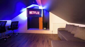 A modern room with a Netflix sign, a sofa, a desk with a chair, and a radiator.