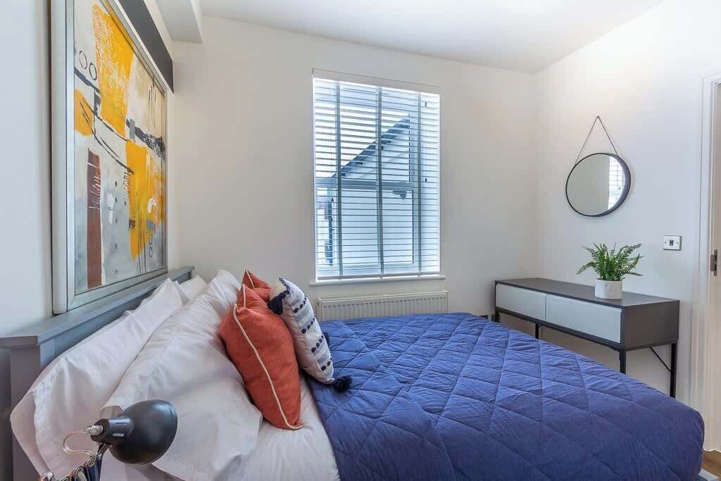 Une chambre à coucher comprenant un lit, une table de chevet, un miroir, une fenêtre avec des stores et un radiateur.