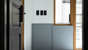 Un pasillo con puerta de madera, un radiador y una ventana con vistas al exterior.
