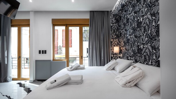 Una habitación de hotel moderna con una cama grande, toallas ordenadamente dobladas, un papel tapiz con motivos de hojas tropicales y vistas a través de una puerta de cristal.