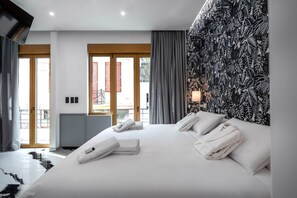 A modern hotel room with a large bed, neatly folded towels, a tropical leaf-patterned wall, and a view through a glass door. - Athens Feeling (Athens)