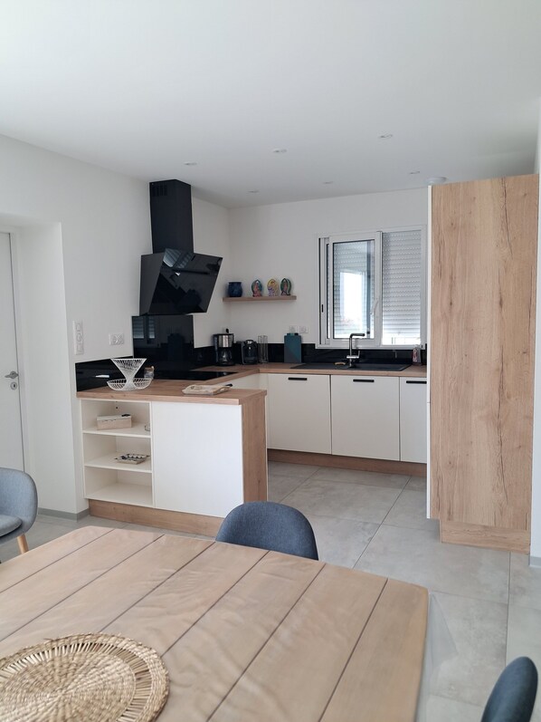 A modern kitchen with white cabinets, a black range hood, and a wooden dining table with chairs.