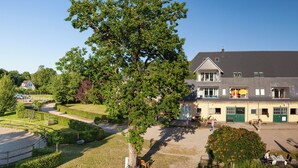 A large building with a symmetrical facade, a central courtyard with a circular gravel area, and a well-maintained lawn. - Hof Eckhorst, Apartment Baltic Sea (Güby)