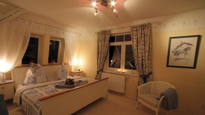 A bedroom with a bed, bedside table, lamp, window with curtains, radiator, and a chair. - Hof Eckhorst, Apartment Baltic Sea (Güby)