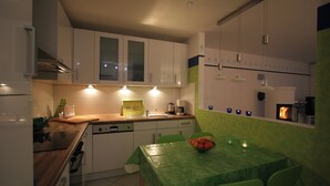 A modern kitchen with white cabinets, a wooden countertop, and a dining area with a green tablecloth. - Hof Eckhorst, Apartment Baltic Sea (Güby)