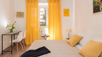 Ein Hotelzimmer mit einem Bett, einem Schreibtisch mit Stühlen, einem kleinen Tisch mit Pflanze und Blick durch große Fenster nach draußen.