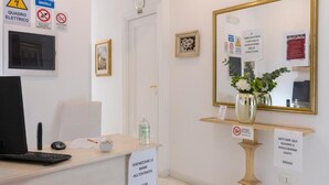 A reception desk with a computer, a chair, and a vase with flowers. There are signs on the wall and a door with the number 502. - Aurelia Home Guest House (Rome)