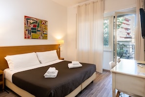 A hotel room with a bed, a desk, a chair, and a view of a traditional building outside. - Aurelia Home Guest House (Rome)