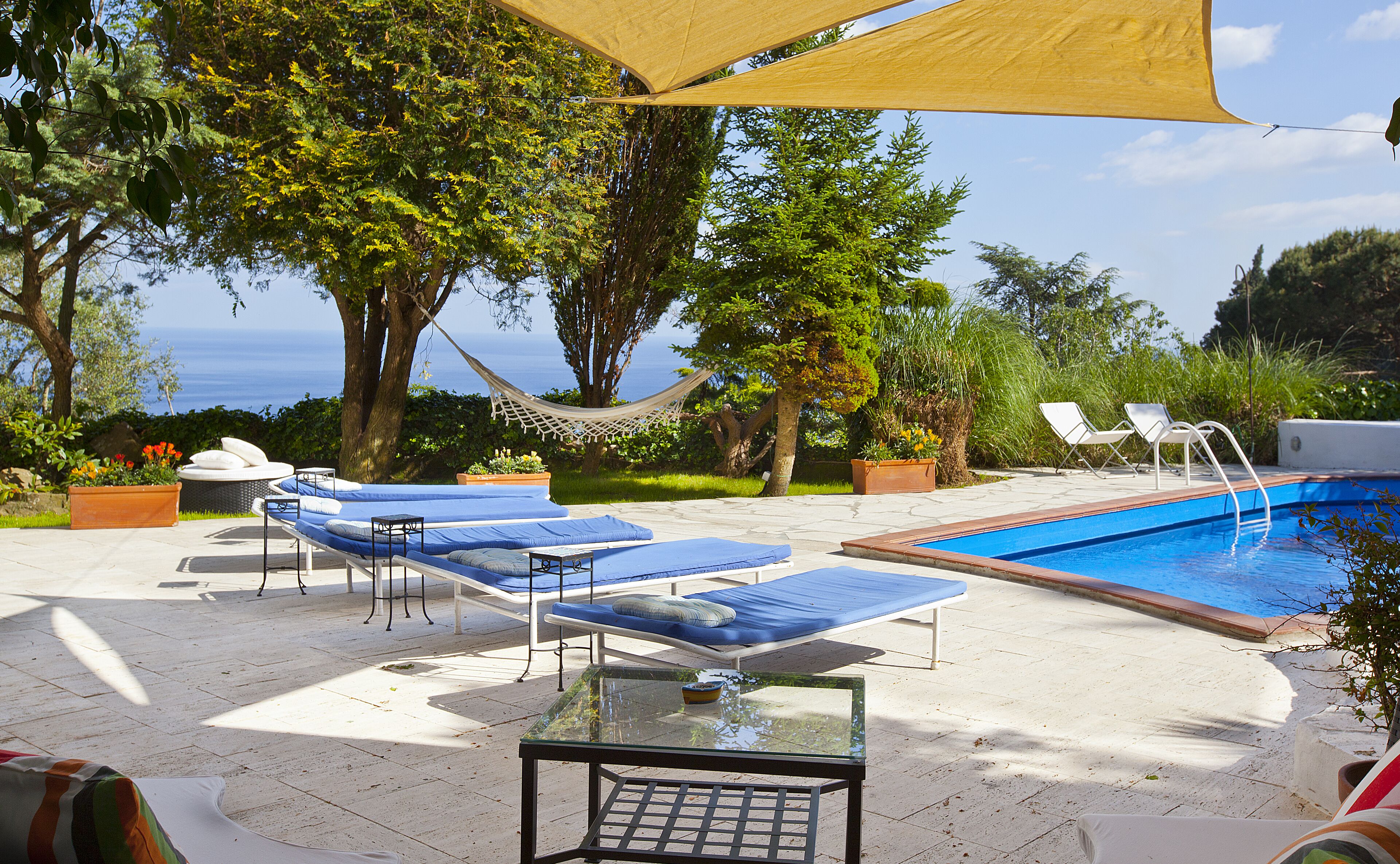 A poolside area with lounge chairs, a hammock, and a glass table.