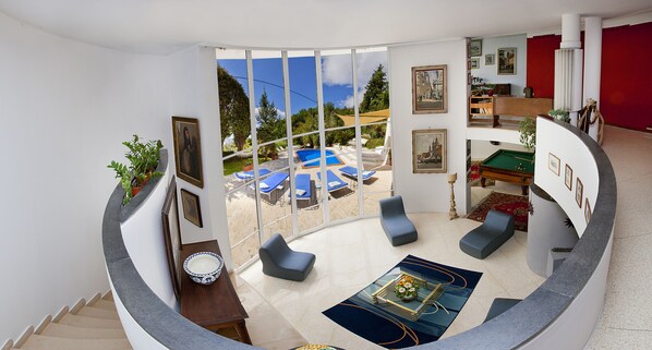 Un salon moderne avec vue sur la piscine, doté de sièges confortables et d’une table de billard.