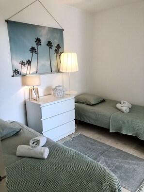 A bedroom with two beds, a dresser, a lamp, and a painting of palm trees. - Calanque --- (Cassis)