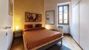 Un dormitorio con cama, mesitas de noche, un radiador y una ventana.