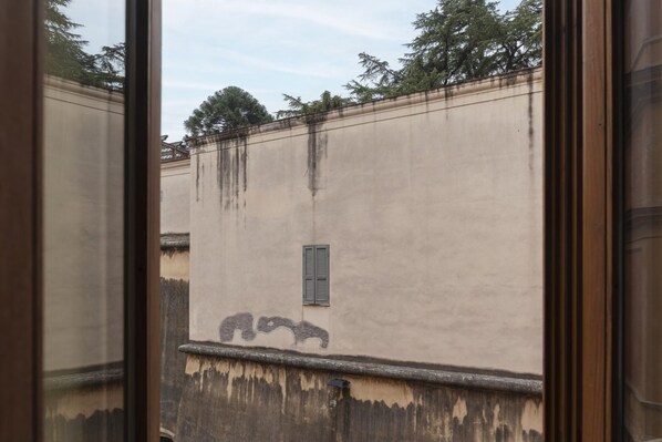 A building with a textured wall, a small window with shutters, and a reflection in the glass.