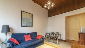 Un salón con un sofá azul, cojines rojos, una mesa con sillas, una lámpara y un cuadro en la pared.