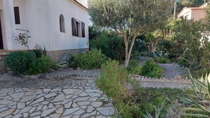 A courtyard with a stone pathway, surrounded by various plants and a white building with windows. - Pretty villa with private pool next to a heavenly cove. (L'Escala)