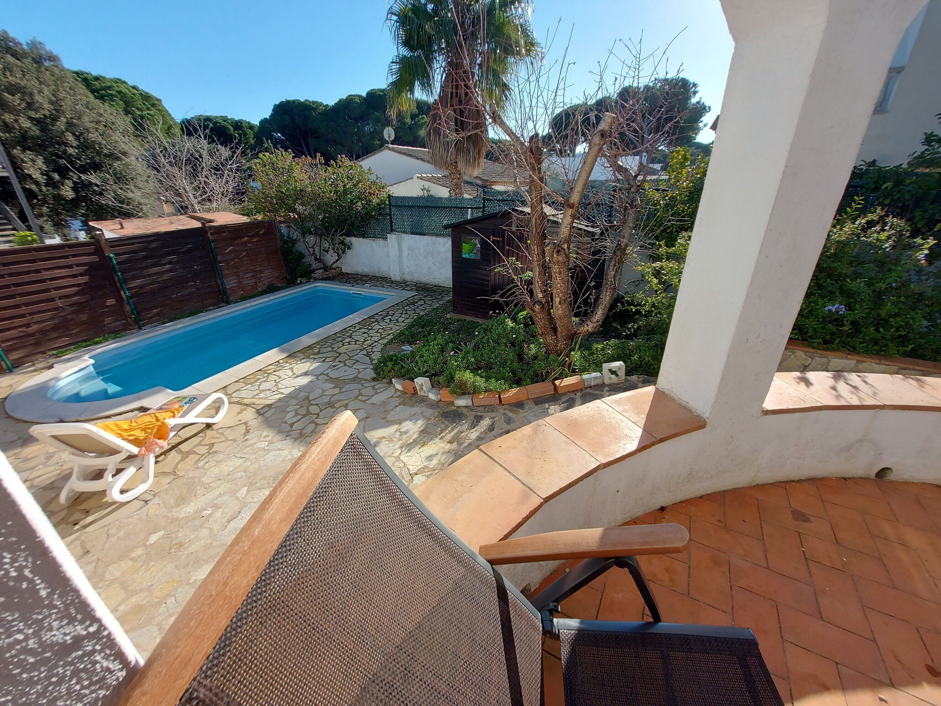 A pool area with a stone deck, lounge chairs, and a small garden with a tree and shrubs.