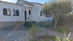 A white building with a stone staircase leading to a door, surrounded by greenery and a cobblestone path. - Pretty villa with private pool next to a heavenly cove. (L'Escala)