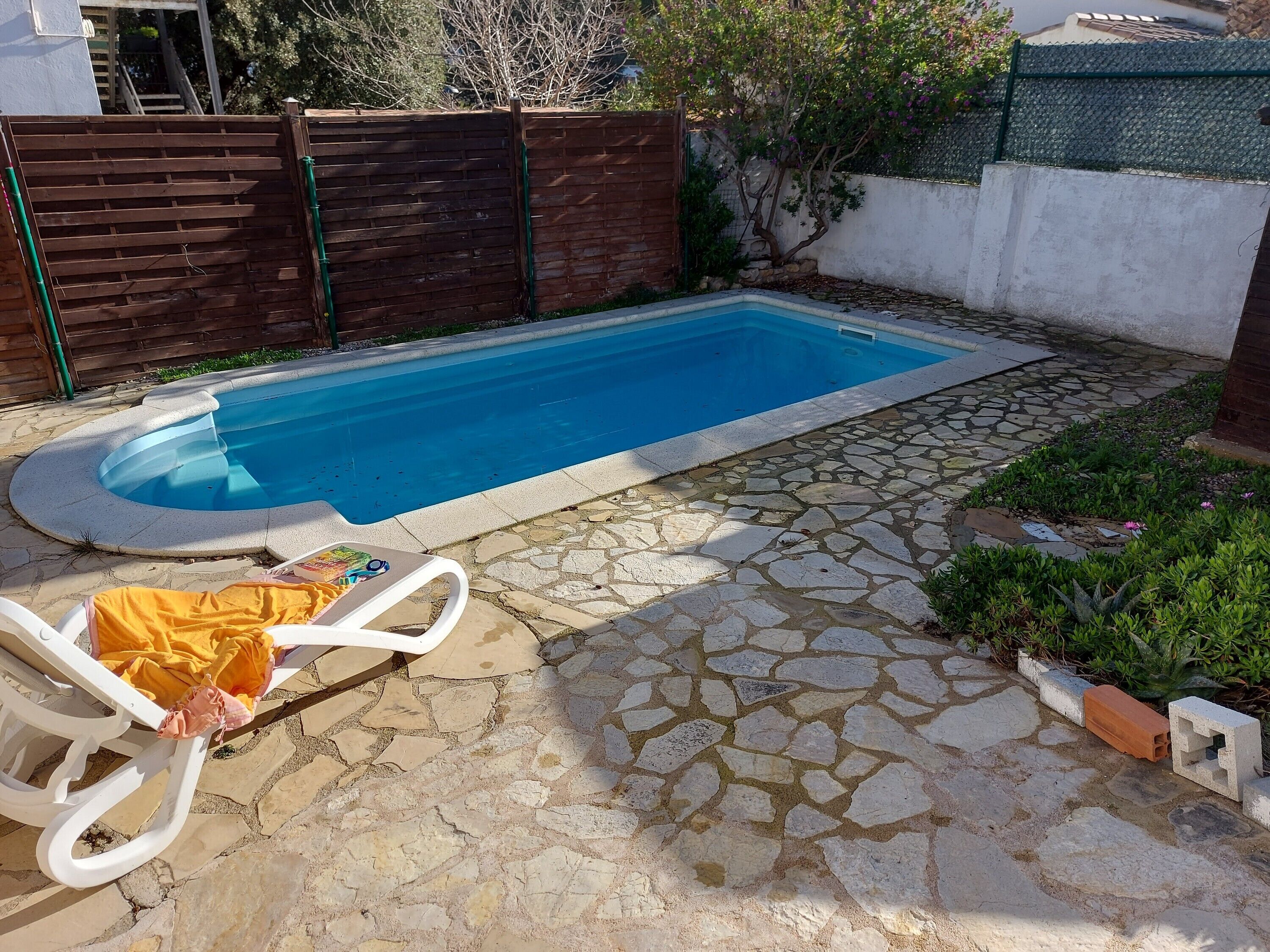 A swimming pool with a stone patio and a lounge chair.