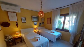 A hotel room with two beds, a hanging light fixture, a window with curtains, and wall-mounted pictures. - Pretty villa with private pool next to a heavenly cove. (L'Escala)