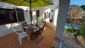 A patio with a table set for dining, a yellow umbrella, and a view of a swimming pool. - Pretty villa with private pool next to a heavenly cove. (L'Escala)