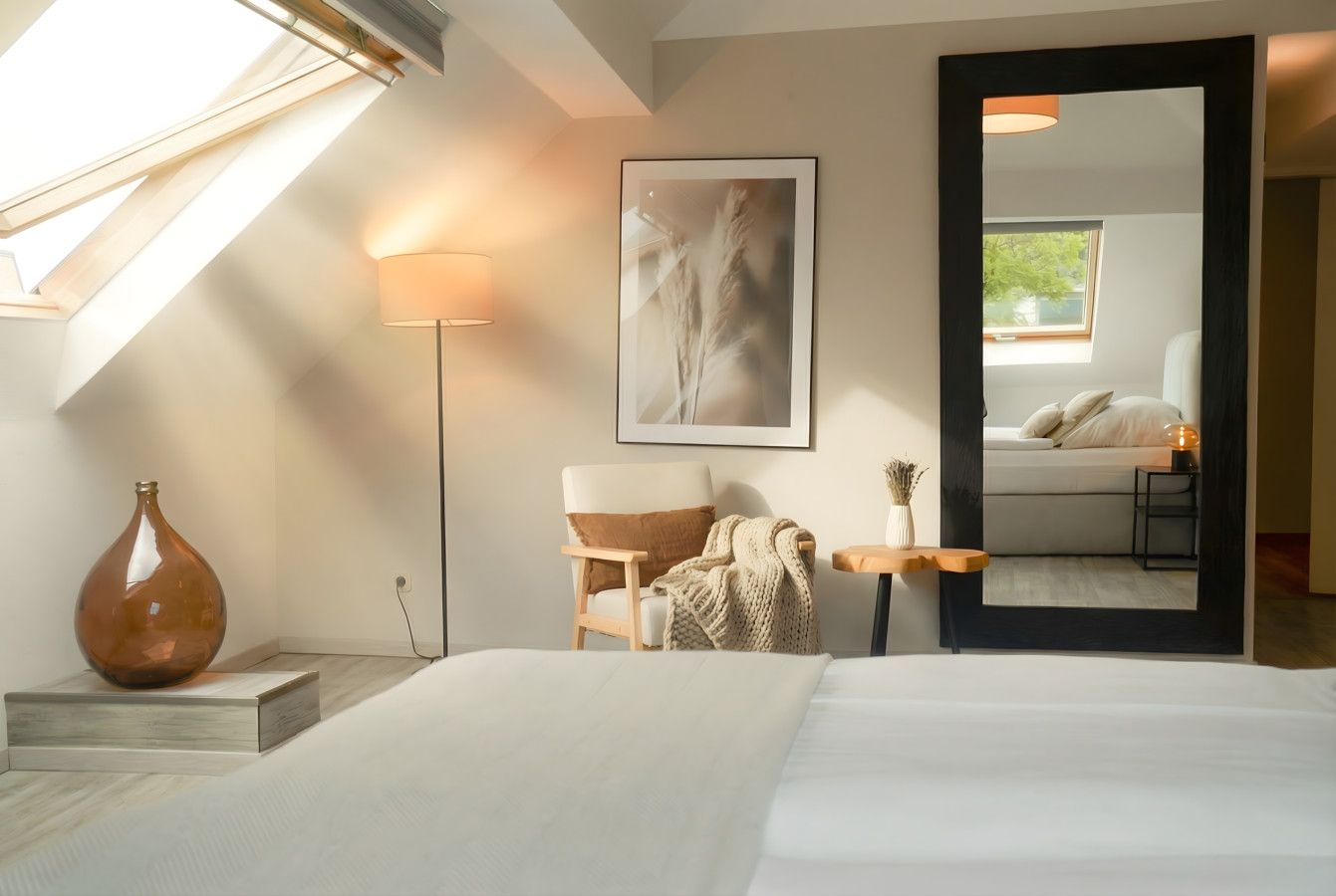 Ein Hotelzimmer mit einem Bett, einer Vase, einer Lampe, einem Sessel, einem Tisch und einem gerahmten Bild an der Wand.