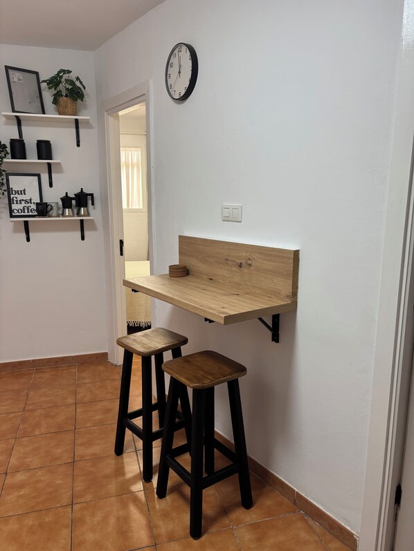 A small kitchen with a wooden countertop, two stools, a clock, and shelves with kitchen items. - Vistamar Suite 158 (Tacoronte)