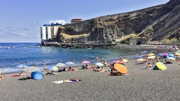 A beach with people sunbathing, umbrellas, and a building on a cliff. - The Vistamar Suite 154 (Tacoronte)