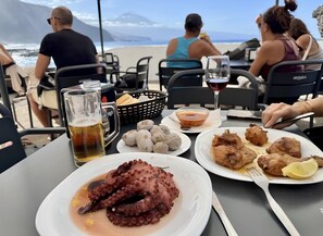 A table with octopus, bread, and a drink, overlooking a beach with people and a mountain in the distance. - Vistamar Suite 158 (Tacoronte)