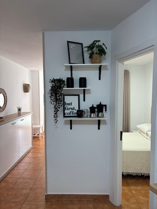 A modern interior with white walls, a wooden cabinet, and a coffee station with a sign. - Vistamar Suite 158 (Tacoronte)
