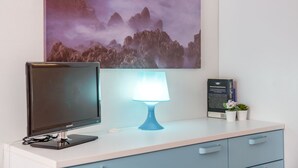 A desk with a computer monitor, a blue desk lamp, a framed informational poster, and a small potted plant.