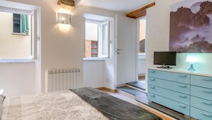 A bedroom with a bed, a dresser, a television, and a painting on the wall.