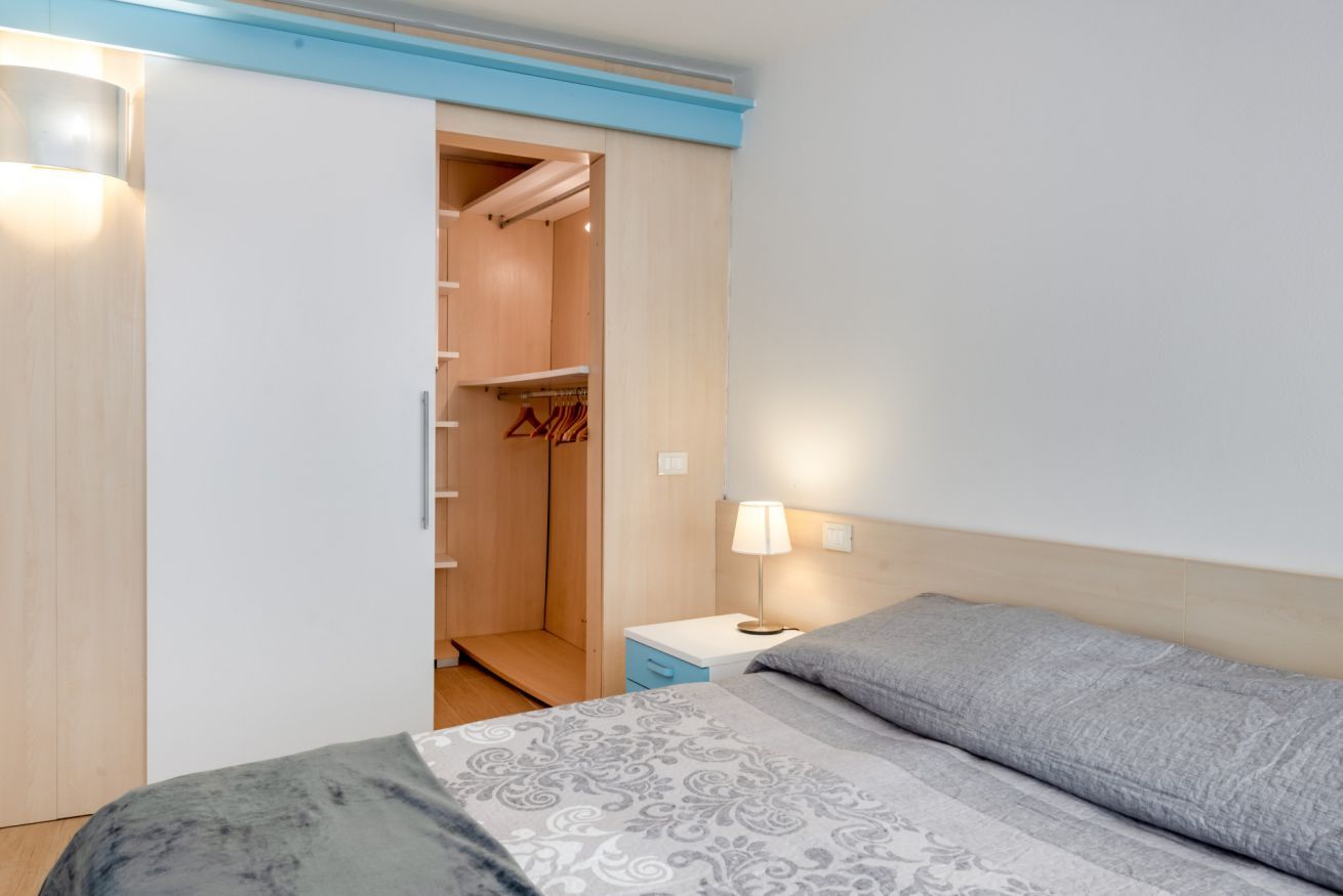 A bedroom with a bed, a nightstand, a bedside lamp, a wardrobe, and a closet.