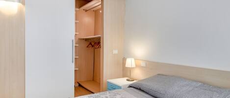 A bedroom with a bed, a nightstand, a bedside lamp, a wardrobe, and a closet.