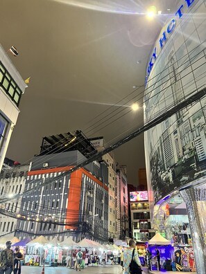 A busy urban street with a prominent hotel sign, market stalls, and a variety of buildings.