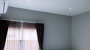 A hotel room with two beds, a window with sheer curtains, and a ceiling-mounted air conditioning unit. - Aowmana Hotel (Bangkok)