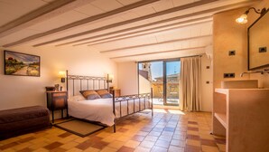 Een slaapkamer met een bed, nachtkastjes, een badkamer met een wastafel en een balkon met uitzicht.