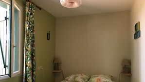 Ein Schlafzimmer mit einem Bett, zwei Nachttischen mit Lampen, einem Fenster mit Vorhängen und einem an der Wand befestigten Regal.